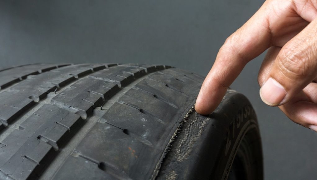 Finger pointing to damage on tire tread. Tire tread problems by tire pressure improper, Wheel alignment Des pneus usés