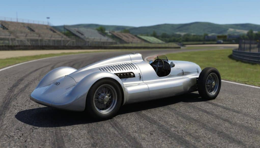 Voiture de course classique Auto Union argentée sur une piste de circuit automobile avec des tribunes en arrière-plan.