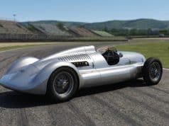Auto Union Lucca : la renaissance d’une Flèche d’argent Voiture de course classique Auto Union argentée sur une piste de circuit automobile avec des tribunes en arrière-plan.