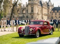 Concours d’élégance automobile : l’art de vivre français Une élégante voiture de sport rouge classique exposée devant un château français avec des hommes en costumes et chapeaux.