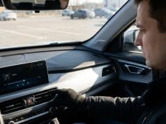 Pourquoi baisser la musique au parking : l’explication Un conducteur portant des gants règle les paramètres multimédia sur l'écran tactile de sa voiture dans un parking.