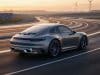 Porsche 911 électrique : la fin du tout-électrique Une Porsche 911 grise roulant sur une piste sinueuse au coucher du soleil, entourée de panneaux solaires et d'éoliennes.