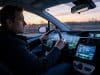 Fatigue technologique en voiture : la surcharge cognitive Un conducteur concentré au volant d'une voiture moderne entouré de multiples écrans numériques lumineux au crépuscule.