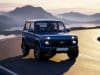 Lada niva airbag : une révolution pour le modèle 2026 Une Lada Niva bleue moderne circulant sur une route côtière sinueuse au coucher du soleil avec des montagnes en arrière-plan.