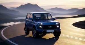 Lada niva airbag : une révolution pour le modèle 2026 Une Lada Niva bleue moderne circulant sur une route côtière sinueuse au coucher du soleil avec des montagnes en arrière-plan.