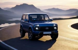 Lada niva airbag : une révolution pour le modèle 2026 Une Lada Niva bleue moderne circulant sur une route côtière sinueuse au coucher du soleil avec des montagnes en arrière-plan.