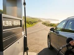Prix du carburant cet été : prévisions pour vos vacances Gros plan sur une main faisant le plein d'une voiture dans une station-service avec une route côtière en arrière-plan.