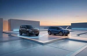 JLR : une stratégie hybride pour le Defender et l’Evoque Un Land Rover Defender et un Range Rover Evoque garés sur des plateformes lumineuses dans un décor architectural moderne.