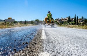 Lait de chaux et routes : la solution face à la canicule Un ouvrier en engin pulvérise du lait de chaux blanc sur une route sombre pour réduire la chaleur lors d'une canicule.