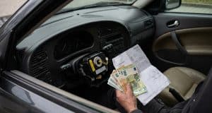 Rappel airbag Takata Saab : la facture s’alourdit en France Une main tenant des billets en euros et une facture à l'intérieur d'une voiture Saab avec un airbag démonté.