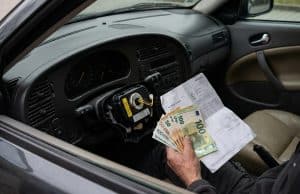 Rappel airbag Takata Saab : la facture s’alourdit en France Une main tenant des billets en euros et une facture à l'intérieur d'une voiture Saab avec un airbag démonté.