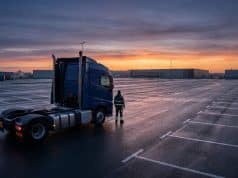 Pénurie chauffeurs routiers : analyse d’une crise mondiale Un chauffeur routier debout face à son camion garé sur un immense parking logistique vide au lever du soleil.
