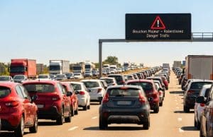 Prévisions Bison Futé : trafic noir les 10 et 11 juillet Vue arrière d'un important embouteillage sur une autoroute sous un ciel bleu avec un panneau d'avertissement lumineux.