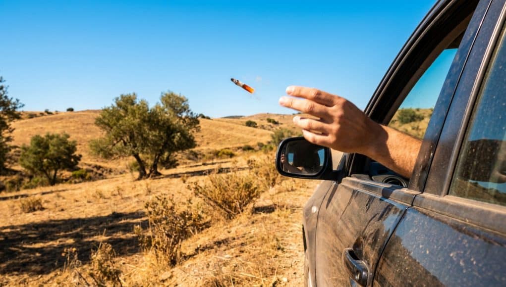 Amende pour jet de mégot en Espagne Une main lance un mégot de cigarette allumé par la fenêtre d'une voiture dans un paysage aride.