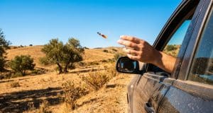 Amende jet mégot Espagne : 500 € et 6 points de retrait Une main lance un mégot de cigarette allumé par la fenêtre d'une voiture dans un paysage aride.