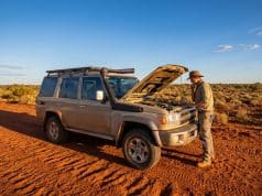 Fiabilité du Toyota Land Cruiser 70 : l’enjeu du moteur 2.8L Un homme examine le moteur de son Toyota Land Cruiser 70 beige sur une piste en terre rouge dans le désert australien.