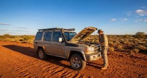 Fiabilité du Toyota Land Cruiser 70 : l’enjeu du moteur 2.8L Un homme examine le moteur de son Toyota Land Cruiser 70 beige sur une piste en terre rouge dans le désert australien.