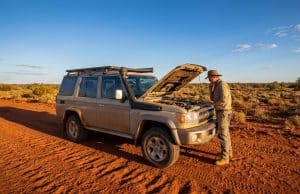 Fiabilité du Toyota Land Cruiser 70 : l’enjeu du moteur 2.8L Un homme examine le moteur de son Toyota Land Cruiser 70 beige sur une piste en terre rouge dans le désert australien.