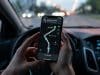 Le mode secret de Google Maps pour la batterie du Pixel 10 Mains tenant un smartphone affichant une interface de navigation GPS simplifiée sur fond sombre à l'intérieur d'une voiture.