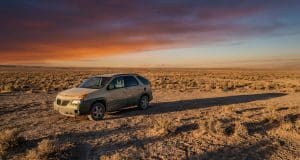 La Pontiac Aztek de Walter White : un choix artistique Une Pontiac Aztek beige stationnée seule dans un désert aride sous un coucher de soleil orange et violet.