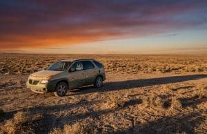 La Pontiac Aztek de Walter White : un choix artistique Une Pontiac Aztek beige stationnée seule dans un désert aride sous un coucher de soleil orange et violet.