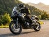 Essai QJ Motor SRT 450 RX : le trail A2 au prix imbattable Un motard en équipement noir chevauche une moto trail QJ Motor SRT 450 RX grise sur une route sinueuse en montagne.