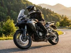 Essai QJ Motor SRT 450 RX : le trail A2 au prix imbattable Un motard en équipement noir chevauche une moto trail QJ Motor SRT 450 RX grise sur une route sinueuse en montagne.