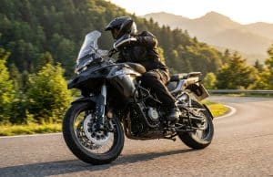 Essai QJ Motor SRT 450 RX : le trail A2 au prix imbattable Un motard en équipement noir chevauche une moto trail QJ Motor SRT 450 RX grise sur une route sinueuse en montagne.