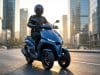 Yamaha Tricity 300 2026 : l’airbag au service de votre sécurité Un pilote à moto sur un scooter à trois roues Yamaha Tricity bleu circulant dans un quartier d'affaires au coucher.