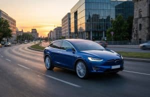 Ventes Tesla Model Y en Europe : analyse d’un succès majeur Une voiture électrique Tesla bleue roulant sur une route urbaine moderne au coucher du soleil.