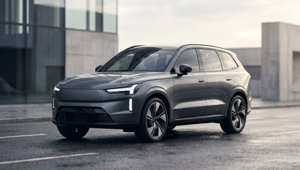 Le SUV électrique gris Volvo EX90 stationné sur une route mouillée devant un bâtiment moderne.