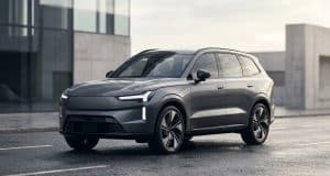 Volvo EX90 lidar abandon : les causes d’un échec technique Le SUV électrique gris Volvo EX90 stationné sur une route mouillée devant un bâtiment moderne.