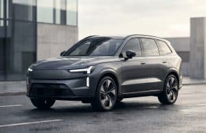 Volvo EX90 lidar abandon : les causes d’un échec technique Le SUV électrique gris Volvo EX90 stationné sur une route mouillée devant un bâtiment moderne.