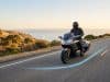 Les nouvelles fonctionnalités Waze optimisent la sécurité Un motard équipé circulant sur une route côtière avec un tracé lumineux bleu au sol, symbolisant l'assistance Waze.