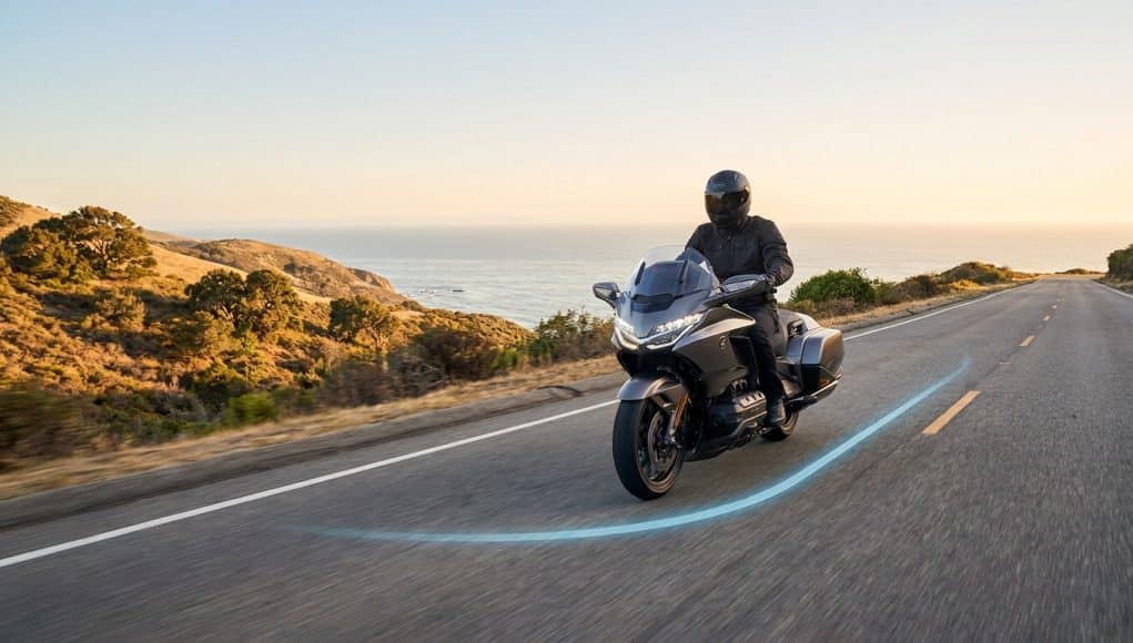 Sécurité routière : Waze protège les motards Un motard équipé circulant sur une route côtière avec un tracé lumineux bleu au sol, symbolisant l'assistance Waze.