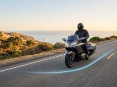 Les nouvelles fonctionnalités Waze optimisent la sécurité Un motard équipé circulant sur une route côtière avec un tracé lumineux bleu au sol, symbolisant l'assistance Waze.