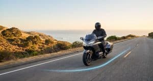 Les nouvelles fonctionnalités Waze optimisent la sécurité Un motard équipé circulant sur une route côtière avec un tracé lumineux bleu au sol, symbolisant l'assistance Waze.
