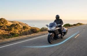 Les nouvelles fonctionnalités Waze optimisent la sécurité Un motard équipé circulant sur une route côtière avec un tracé lumineux bleu au sol, symbolisant l'assistance Waze.