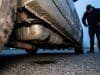 Vol carburant par perforation réservoir : un fléau coûteux Un homme regarde tristement un réservoir de voiture percé laissant fuir du carburant au sol.