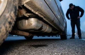 Vol carburant par perforation réservoir : un fléau coûteux Un homme regarde tristement un réservoir de voiture percé laissant fuir du carburant au sol.