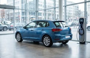 Ventes renault clio 6 : analyse d’un début complexe en 2026 Une voiture bleue stationnée à côté d'une borne de recharge électrique dans une concession automobile vitrée.