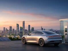 Marché voiture électrique : prévisions et indépendance Voiture électrique moderne en charge devant une skyline urbaine au coucher du soleil avec des panneaux solaires et éoliennes.