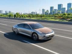 Voiture solaire Luminetta : vers une autonomie énergétique La voiture solaire argentée Luminetta roule sur une route moderne avec des panneaux solaires visibles sur le toit et capot.