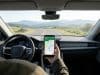 Les meilleures applications pour votre trajet en voiture Main tenant un smartphone avec une application de guidage GPS sur le tableau de bord d'une voiture roulant sur une route.