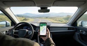 Les meilleures applications pour votre trajet en voiture Main tenant un smartphone avec une application de guidage GPS sur le tableau de bord d'une voiture roulant sur une route.
