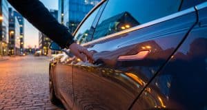 Rappel Tesla en Chine : le défi des poignées de sécurité Gros plan sur une main s'approchant de la poignée affleurante d'une Tesla garée dans une rue urbaine au crépuscule.