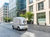 Robot de livraison autonome en France : le nouveau cadre 2026 Un petit robot de livraison blanc autonome circule sur une rue piétonne pavée bordée d'immeubles de bureaux modernes.
