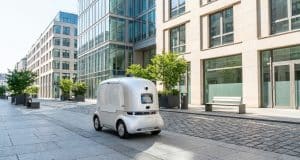 Robot de livraison autonome en France : le nouveau cadre 2026 Un petit robot de livraison blanc autonome circule sur une rue piétonne pavée bordée d'immeubles de bureaux modernes.