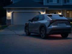 Rappel park outside : le danger d’incendie des véhicules en 2026 Une voiture électrique grise stationnée en extérieur et branchée sur une prise domestique devant une maison la nuit.