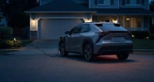 Rappel park outside : le danger d’incendie des véhicules en 2026 Une voiture électrique grise stationnée en extérieur et branchée sur une prise domestique devant une maison la nuit.